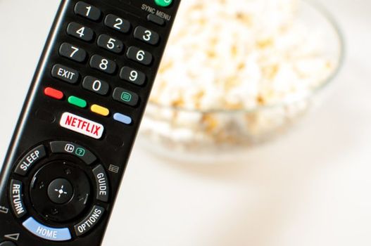 Zagreb, Croatia - March 5, 2016: Remote control smart TV with Netflix button with popcorn in the background.