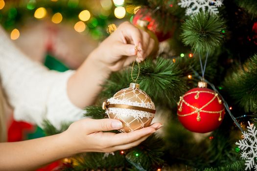 Closeup image of woman in sweater decorating Christmas tree with baubles