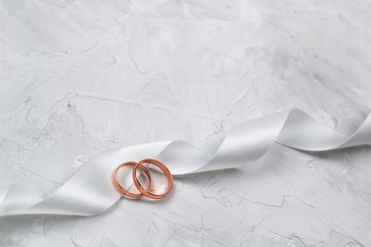 two golden rings and white satin ribbon wedding decor or wedding invitation background concept