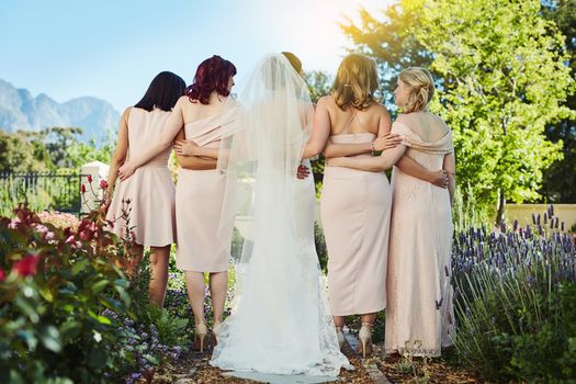 Rearview shot of a young bride and her bride's maids standing together outside during the day