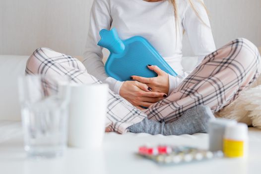 A young girl holds a hot water bottle to her stomach while sitting down.